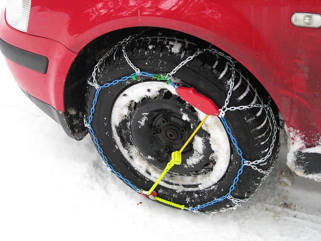 Snow tire chains wrapped around a car tire in the snow.