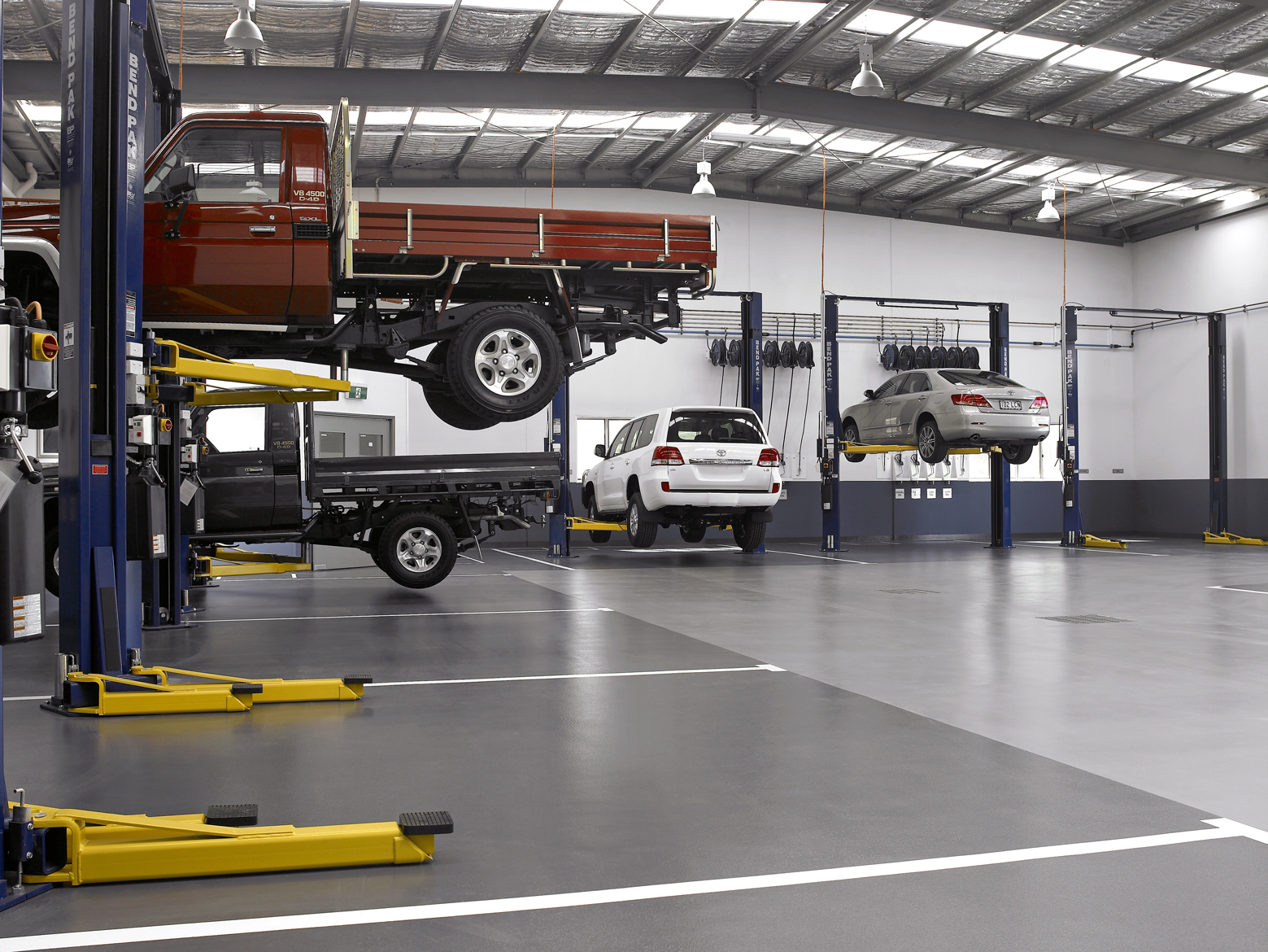 Several BendPak two-post lifts in an open garage space. Trucks, SUVs, and sedans are loaded on the car lifts.